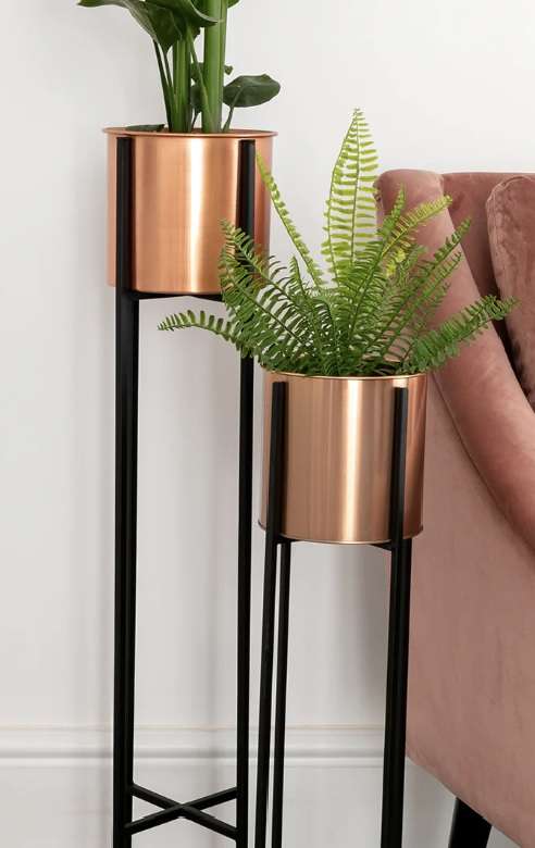 two plant pots on stilts in front on a pink velvet armchair